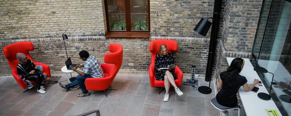 Studenter sitter i fåtöljer och läser inne på Pedagogiska biblioteket